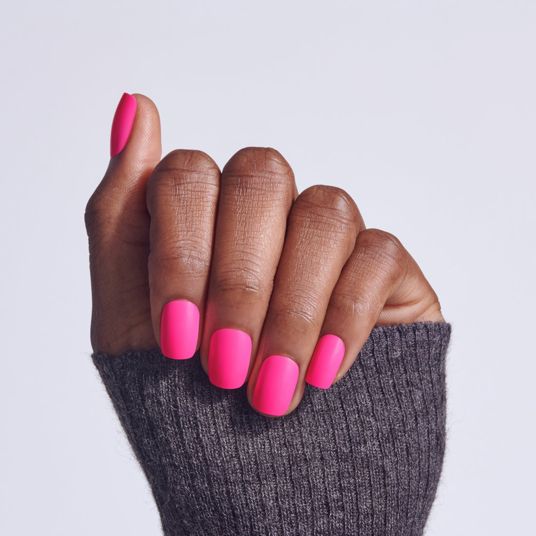 Hand with bright pink nail polish on dark skin tone against gray background