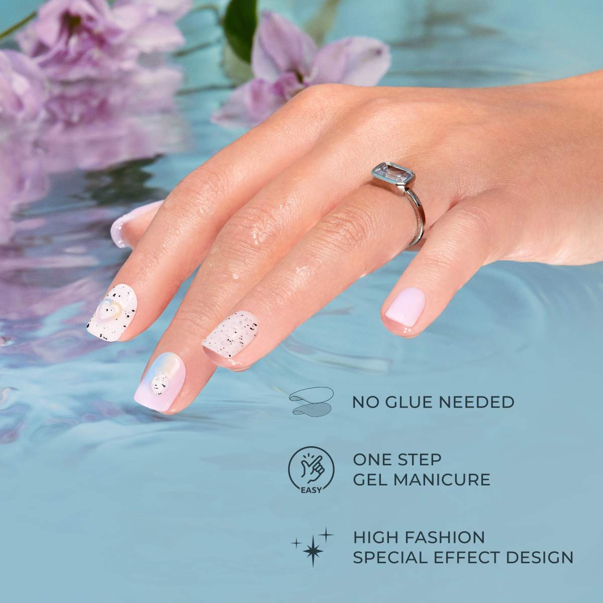 Hand with pastel pink and white press-on nails featuring black speckles and 3D heart accents resting in water, with text highlighting no glue needed, easy one-step gel manicure, and high fashion special effect design.