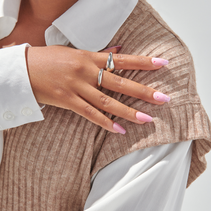 Hand with medium-length, square-shaped press-on nails in soft pink tones; some nails have purple glitter tips and small pink rhinestone accents.