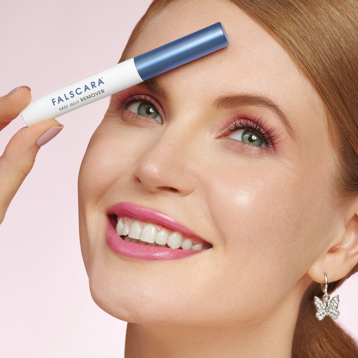 Woman holding a falscara eyelash remover against her face on a pink background