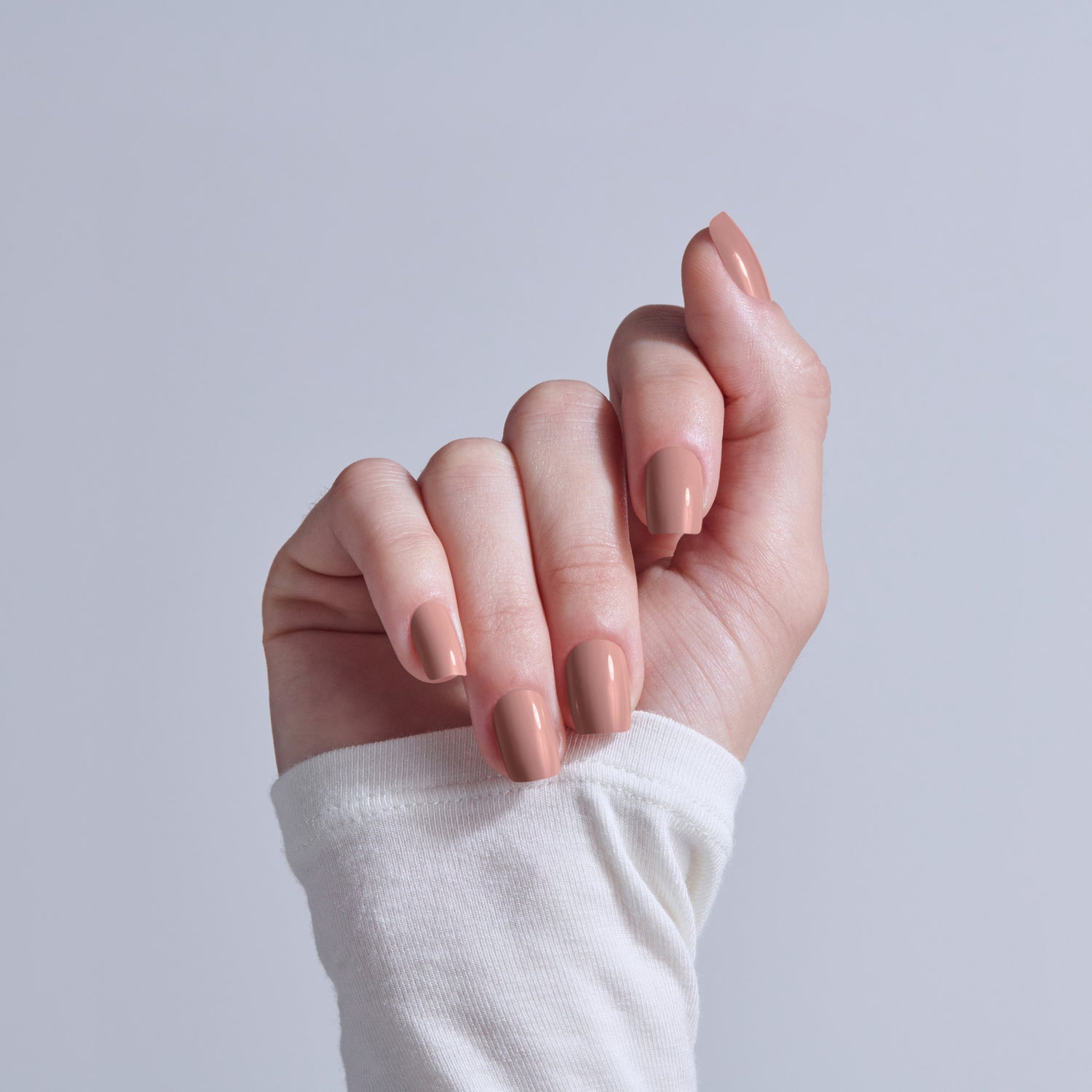 Hand with nude almond-shaped manicure against light blue background