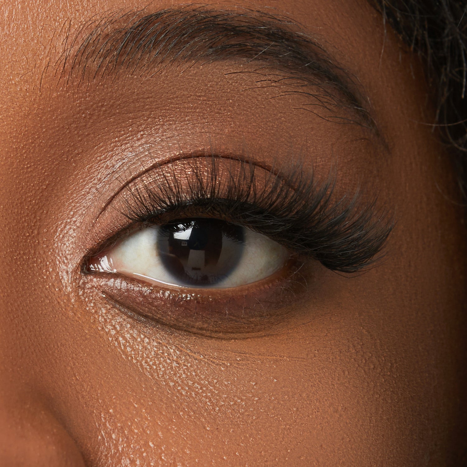 Close-up of eye with voluminous black mascara and defined eyebrow on warm brown skin tone.