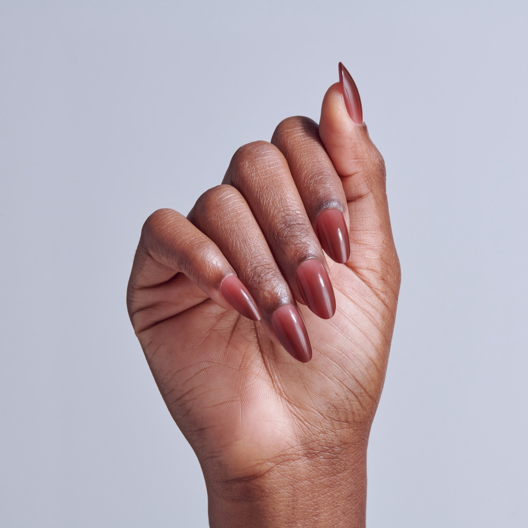 Hand with burgundy almond-shaped nails against light blue background