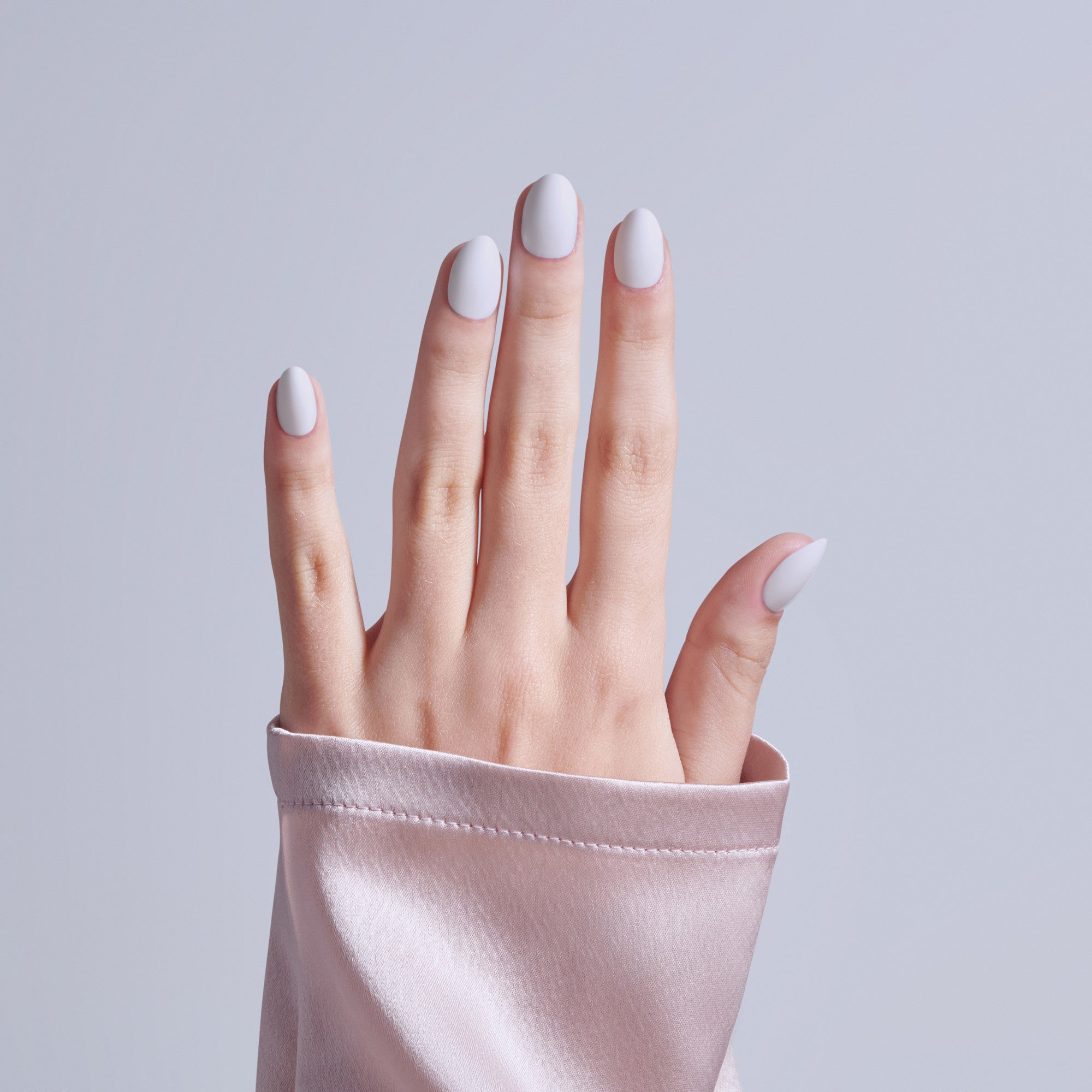 Hand with white oval nails emerging from pink fabric sleeve against gray background.