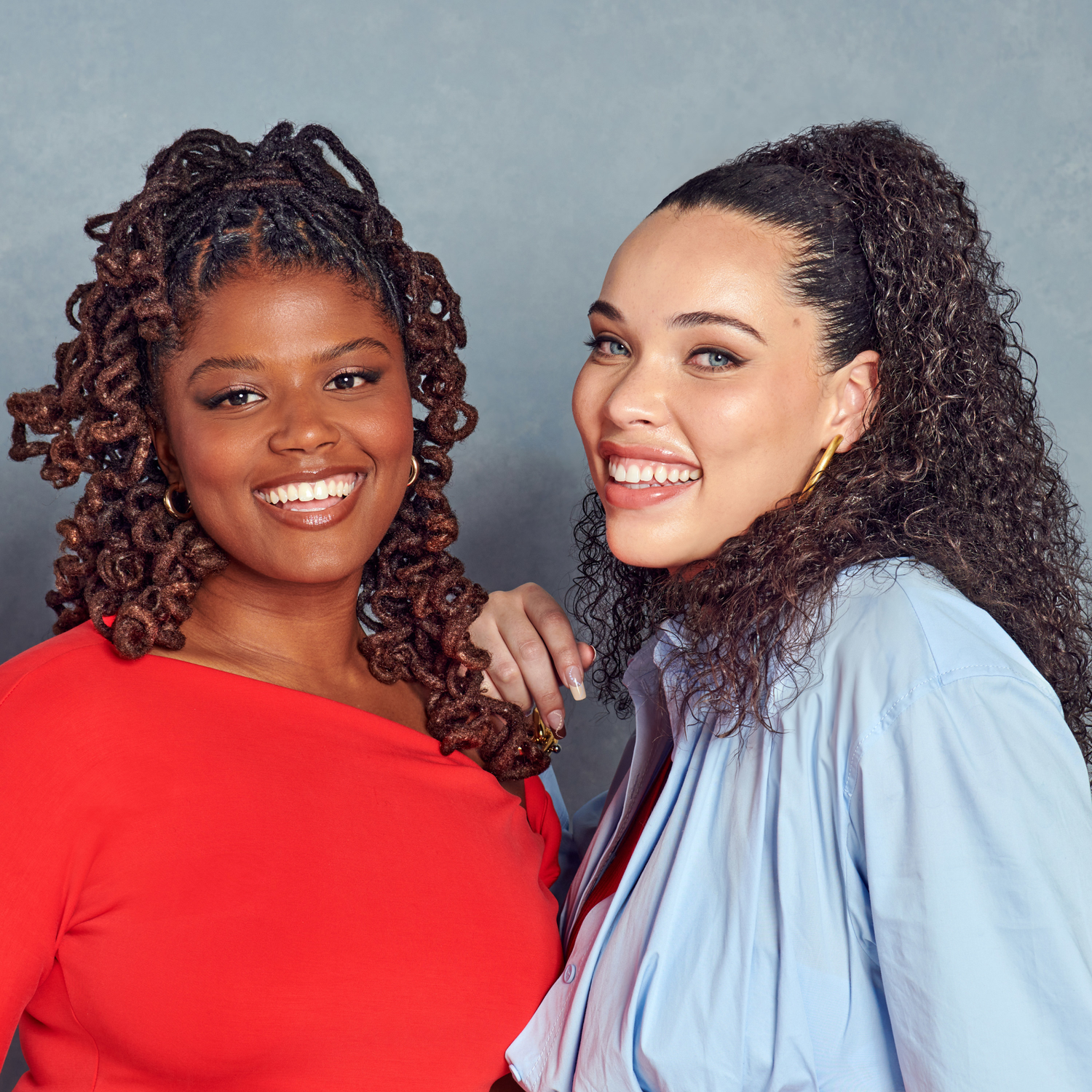 Two women with styled hair smiling against a gray background