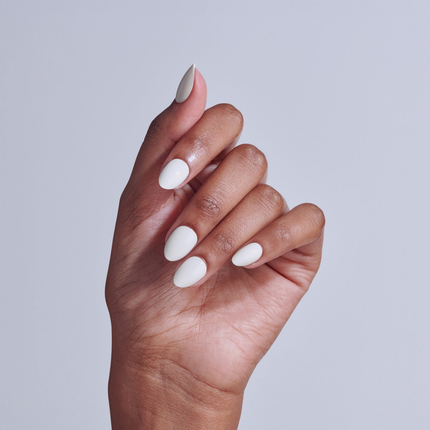 Hand displaying white and nude almond-shaped manicure against gray background.