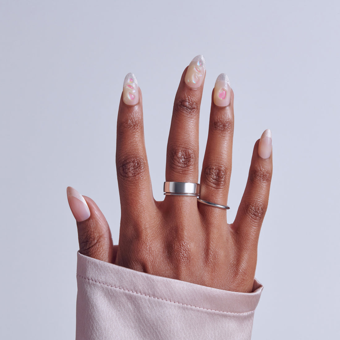 Hand with almond nails featuring white base, pink accents, and glossy finish, wearing silver rings.