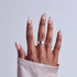 Hand with almond nails featuring white base, pink accents, and glossy finish, wearing silver rings.