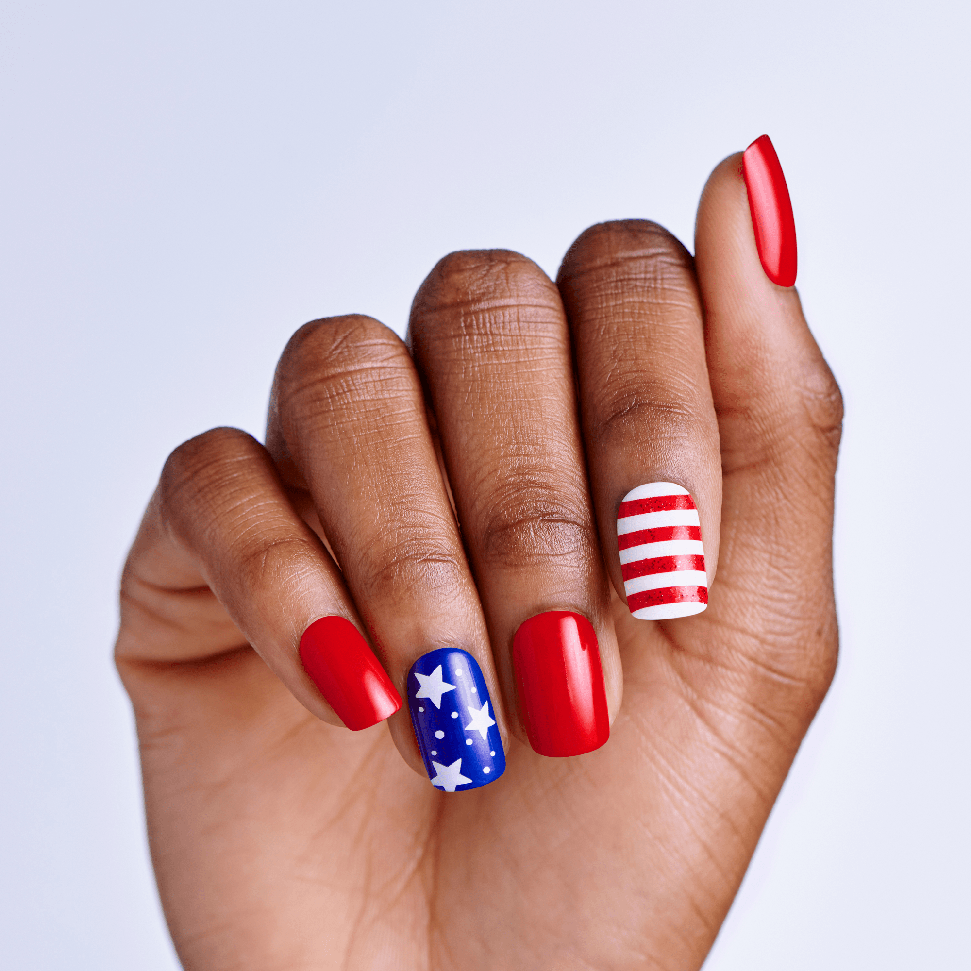 Hand with red, white, and blue press on nails on a light gray background
