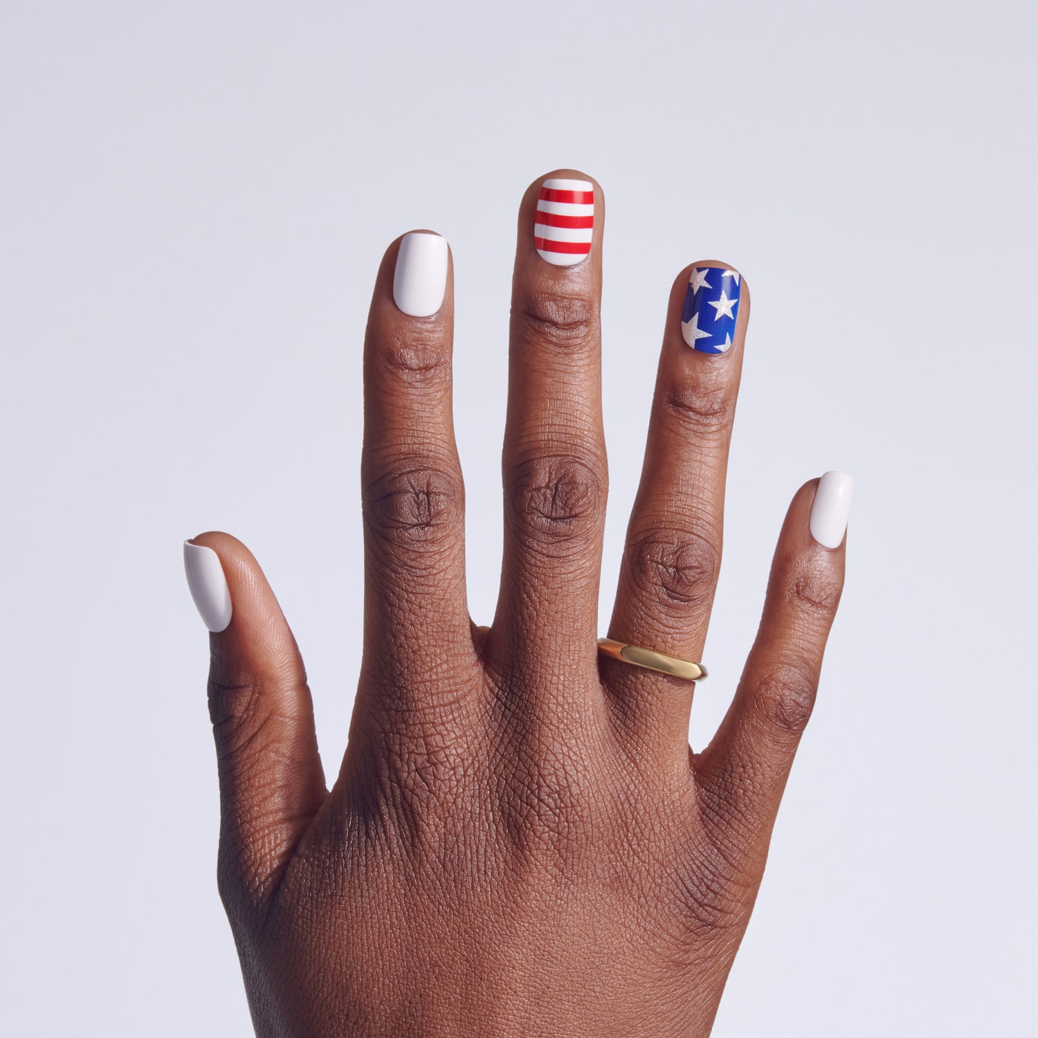 Hand with patriotic nail art: white, red/white stripes, blue with stars.