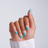 Hand with short squoval teal ombre press-on nails featuring gold chain accent nail art on light gray background