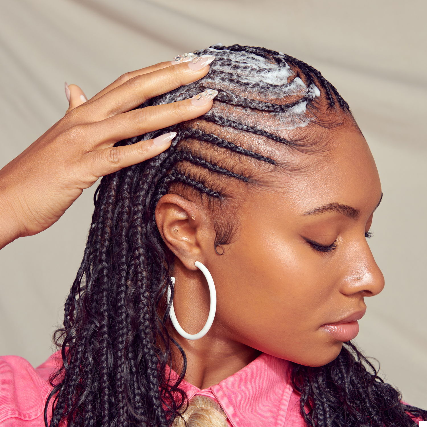 Woman with braided hair applying a product to her scalp against a neutral background