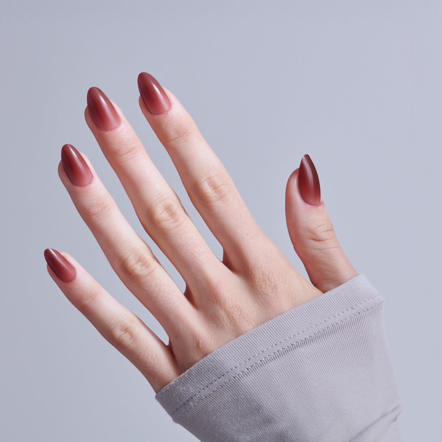 Hand displaying almond-shaped nails with burgundy ombre nail polish against gray background.