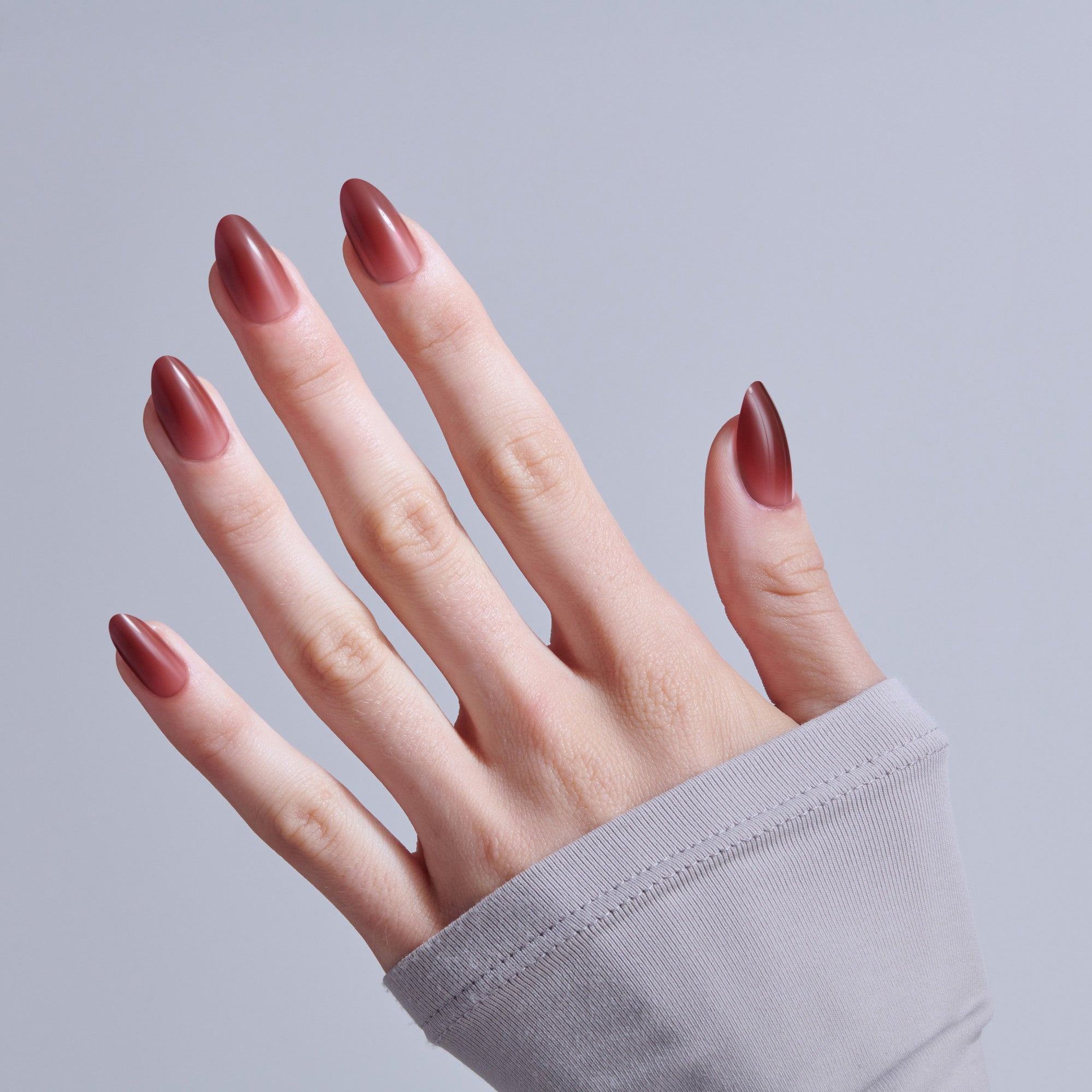 Hand displaying almond-shaped nails with burgundy ombre nail polish against gray background.