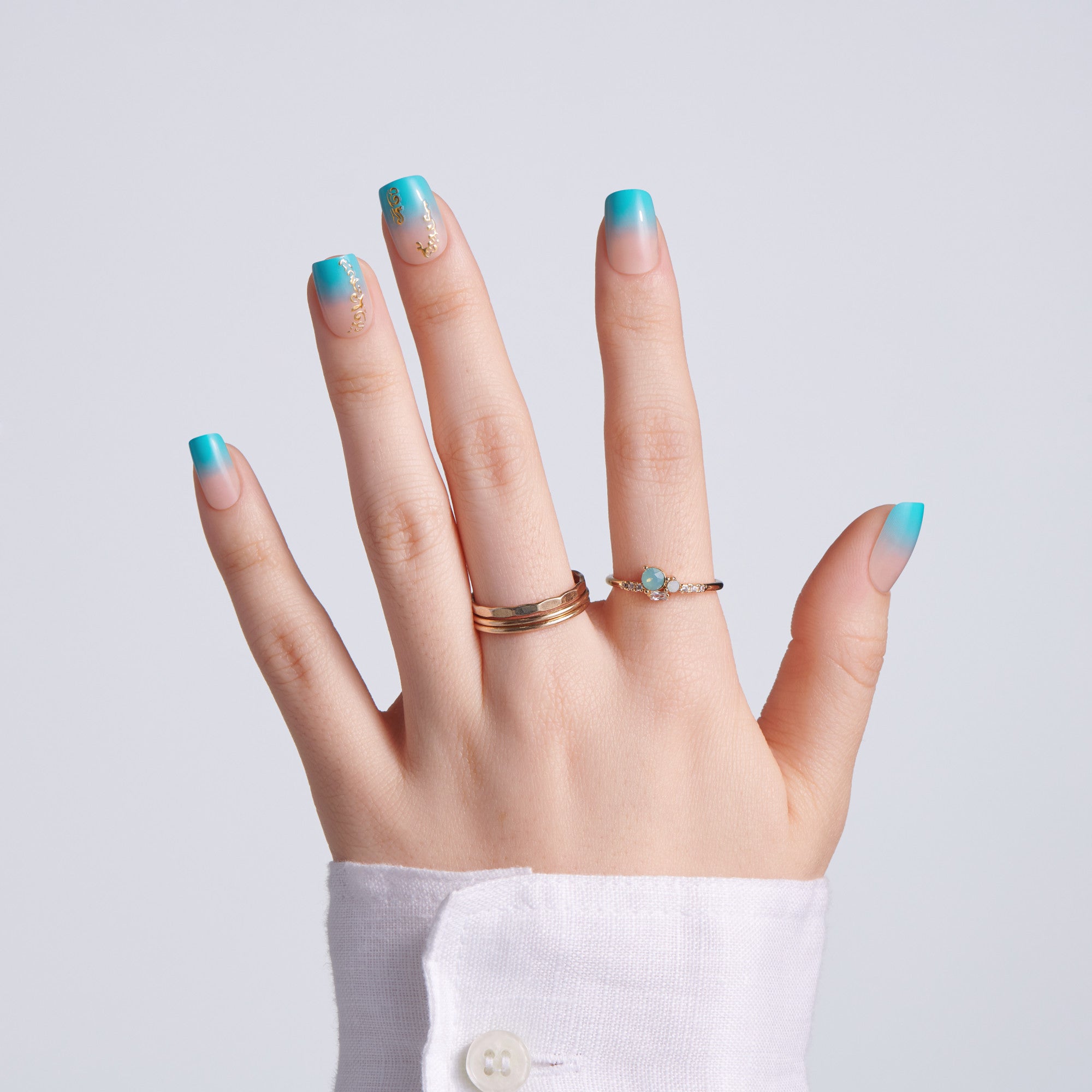 Hand with turquoise nail polish and gold rings on a light gray background