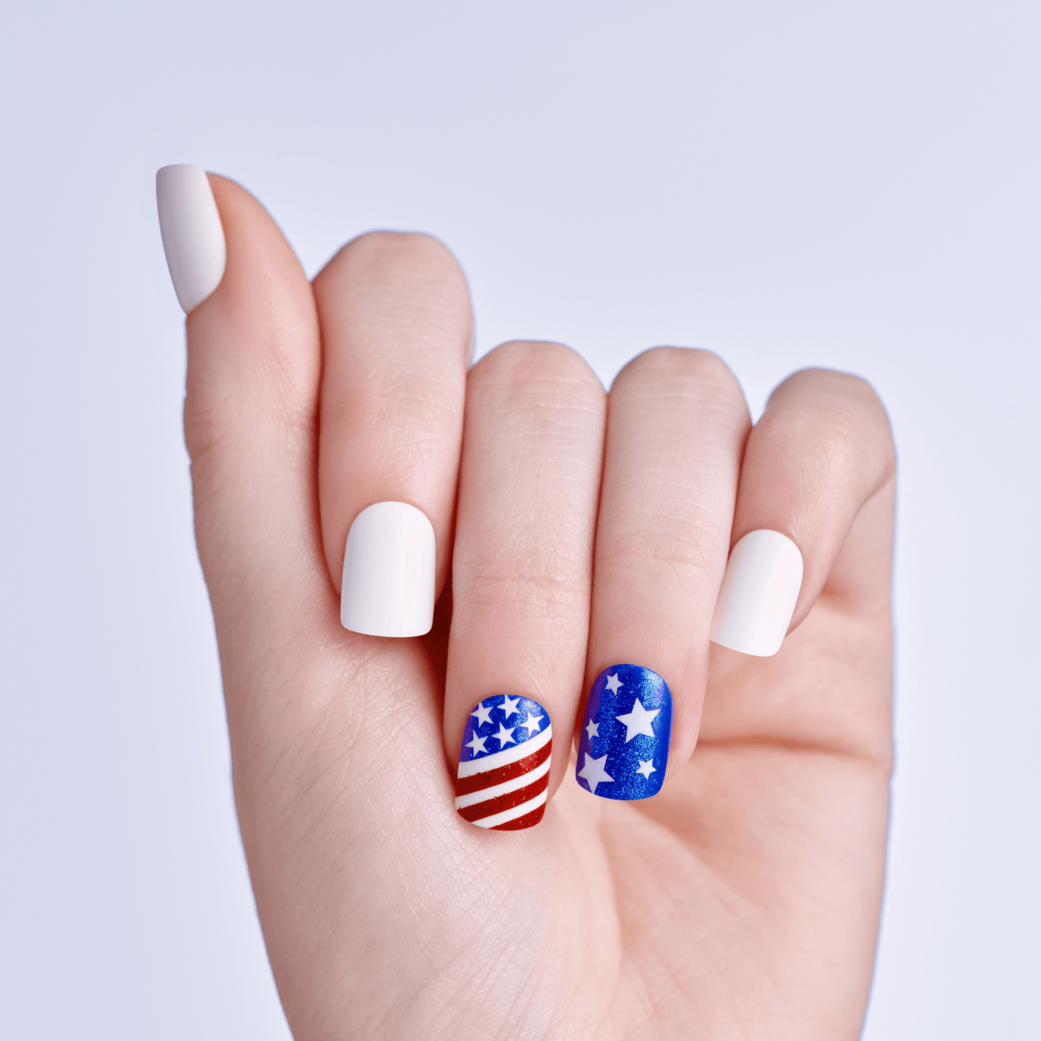 Hand with white nails featuring American flag and star designs on a light gray background