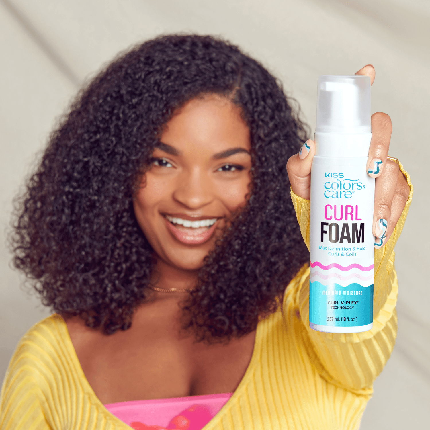 Woman holding KISS Colors &amp; Care Curl Foam bottle, showcasing defined curls.