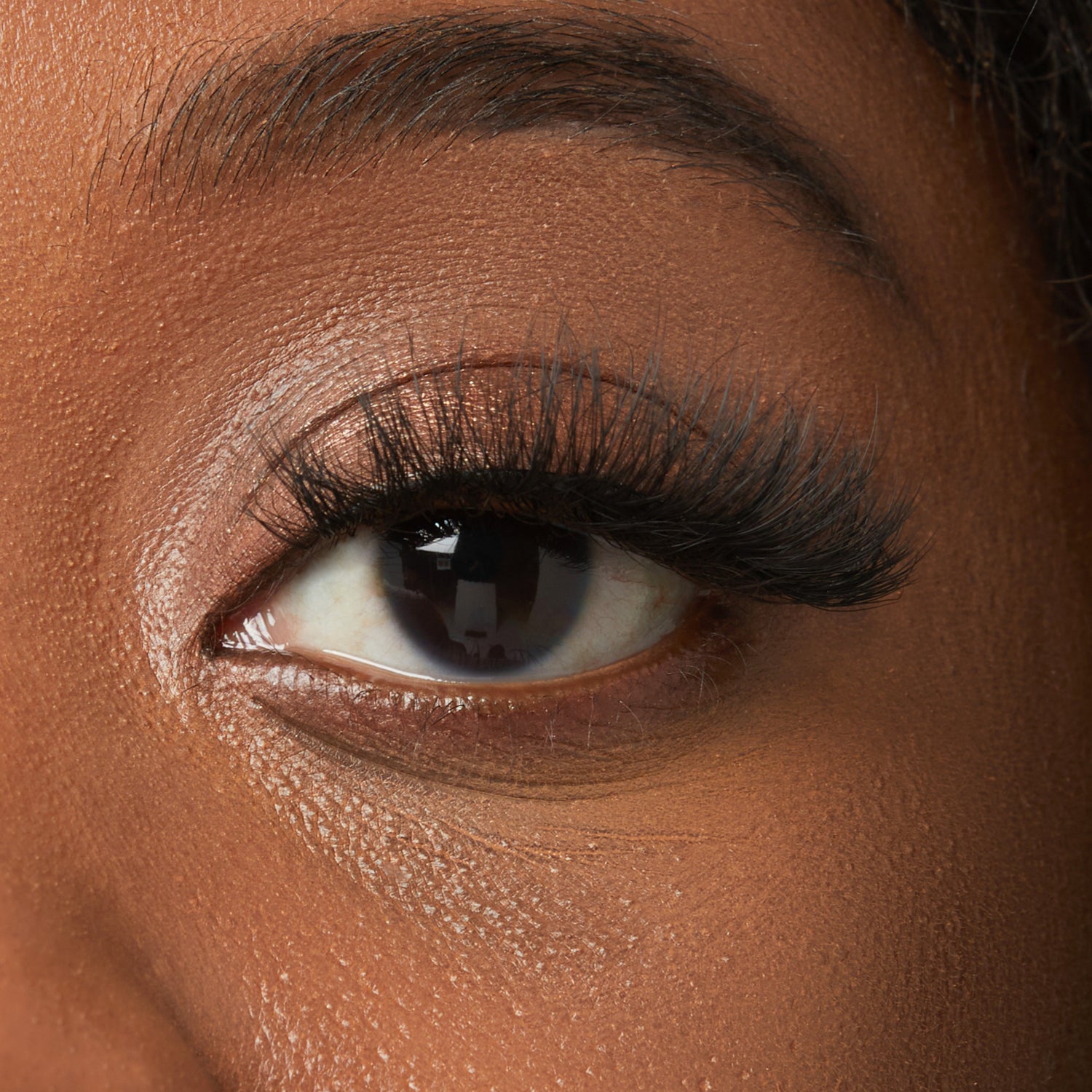 Close-up of eye with voluminous black mascara and shimmery eyeshadow on deep skin tone.