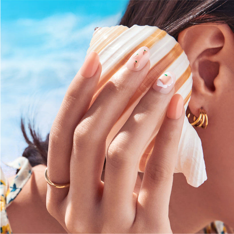 Close-up of manicured nails with peach and white striped design against blue ocean background.