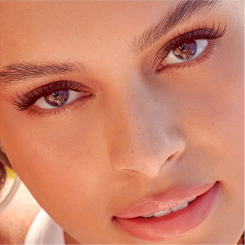 Close-up of woman's face wearing KISS imPRESS Demi Natural false lashes and pink lipstick.