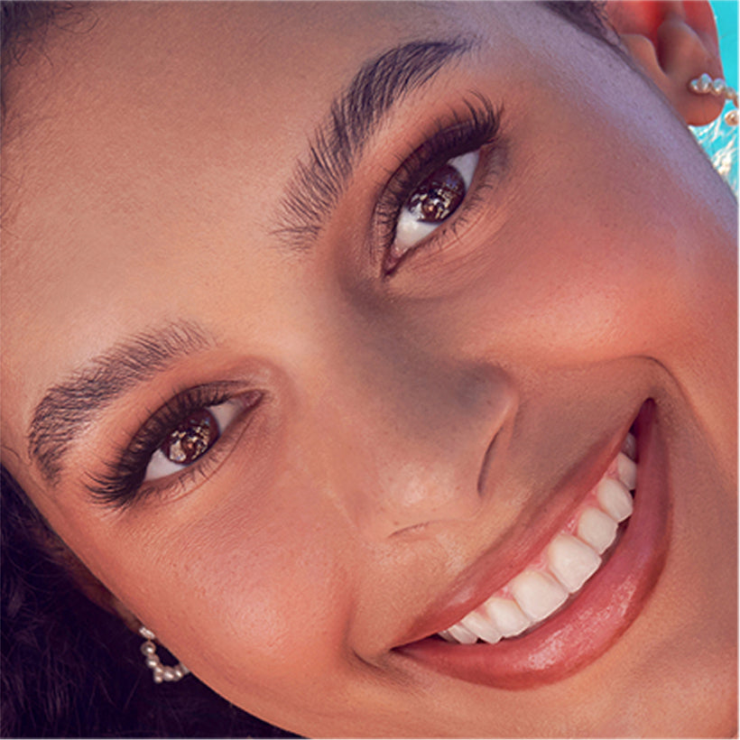 Close-up of woman wearing KISS imPRESS Demi Wispy false lashes, smiling at camera.