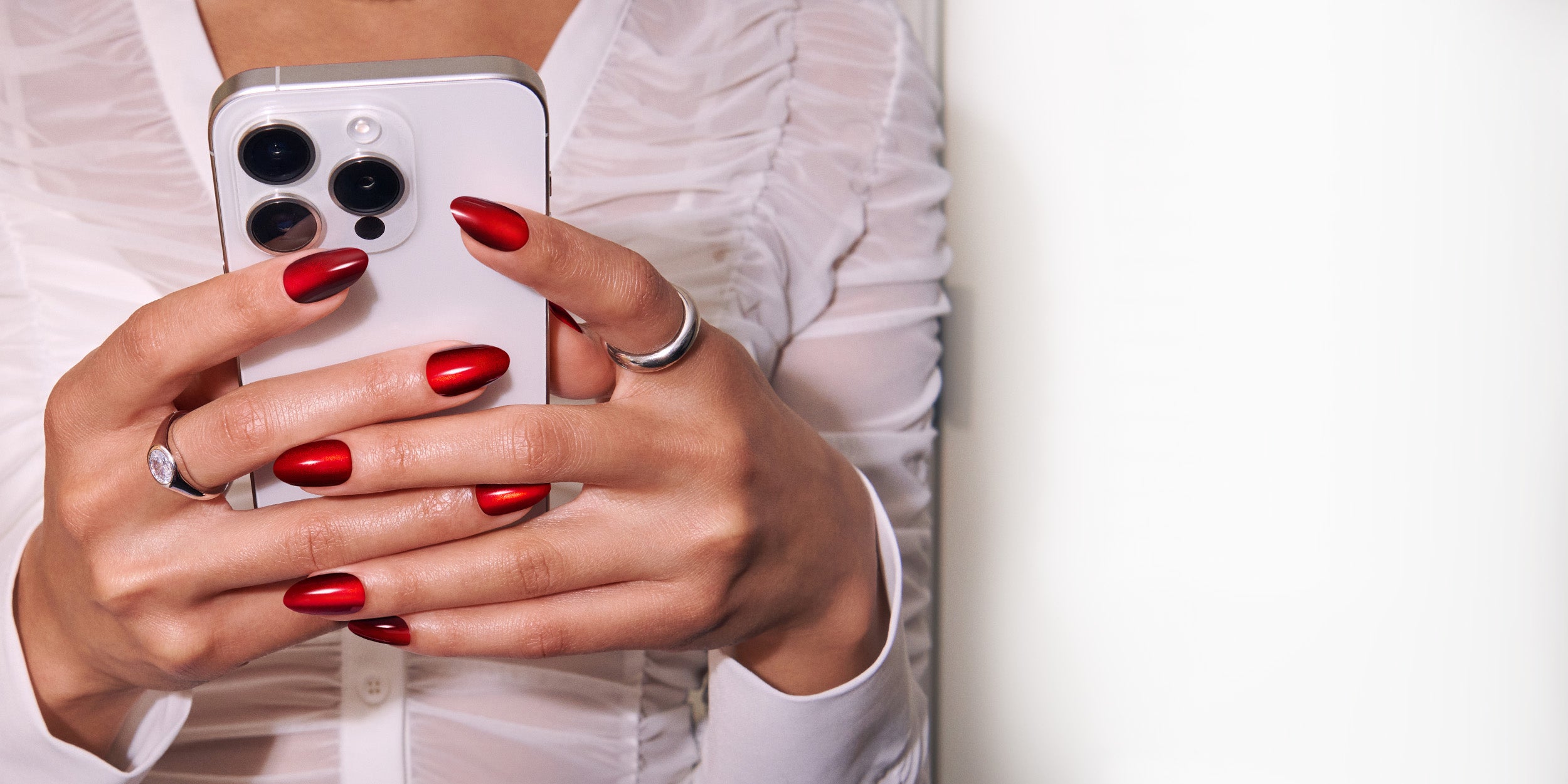 Close-up of hands with red nail polish holding a smartphone against a white background