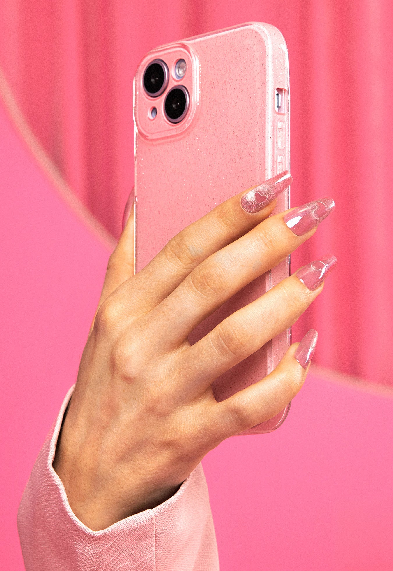 Hand holding a pink phone case against a pink background
