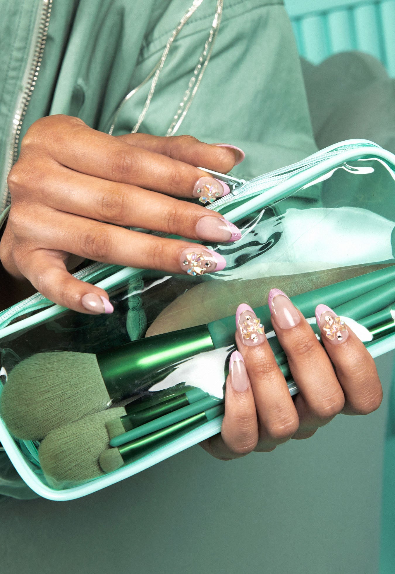 Hand holding a clear makeup bag with green makeup brushes, wearing a green jacket.