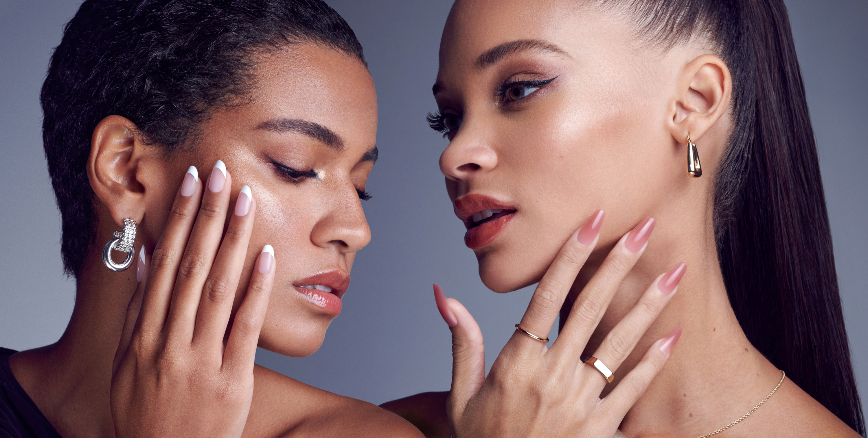 A woman on the left modeling a medium length French nail style and a woman on the right modeling a long length pink-colored nail style.