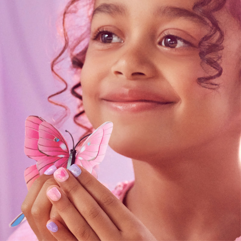 Young child with curled hair holding pink butterfly, pink nail polish, soft pink background