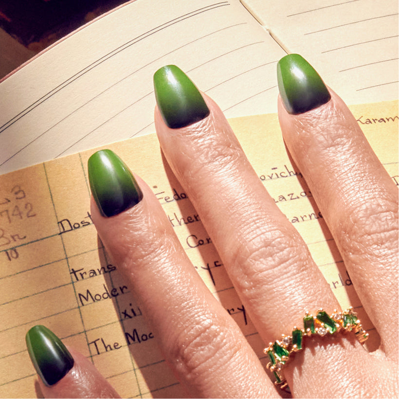Green ombre nail polish on model's fingers over open notebook pages.