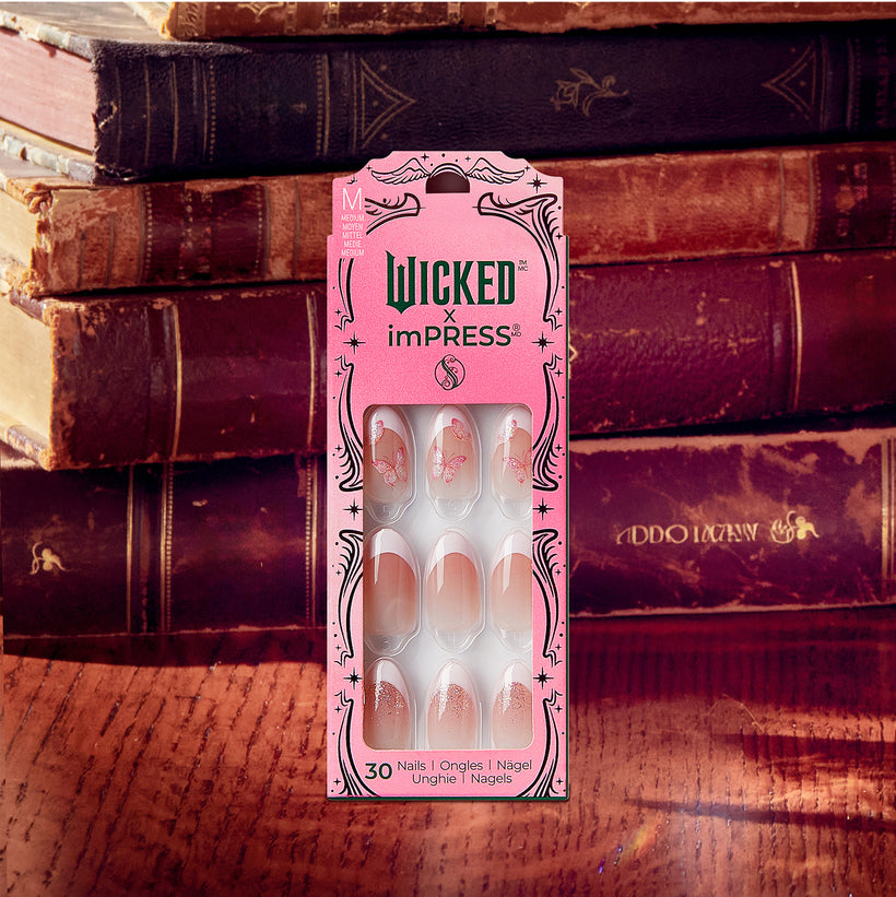Wicked x imPRESS press-on nails in pink packaging against vintage books.