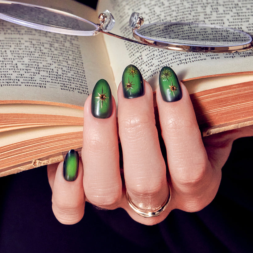 Green ombre nails with gold star designs, displayed with open book and eyeglasses.