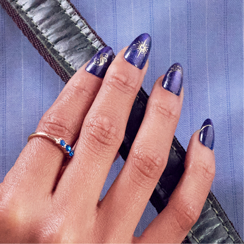 Purple nails with gold sun design and blue gemstone ring on model hand