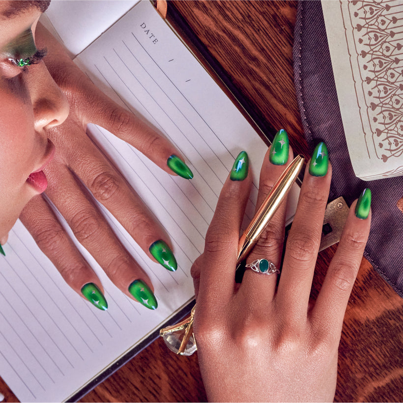 Person with green almond nails holding pen over blank notebook dated page
