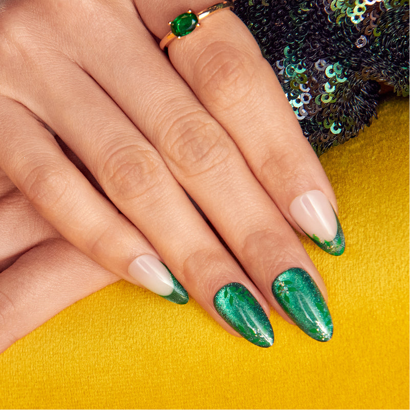 Hand wearing emerald green glitter almond nails with nude tips and green gemstone ring.