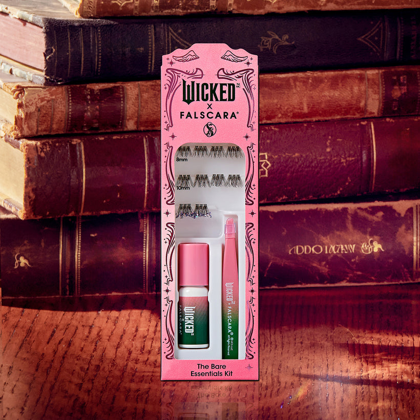 Wicked x Falscara makeup kit with false lashes, mascara, and eyeliner on antique books.