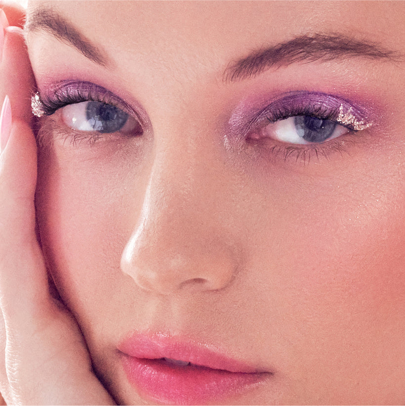 Close-up of woman's face with purple eyeshadow, glitter eyeliner, and pink lips.