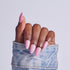 Hand with pink almond-shaped acrylic nails in light blue denim cuff against white background.