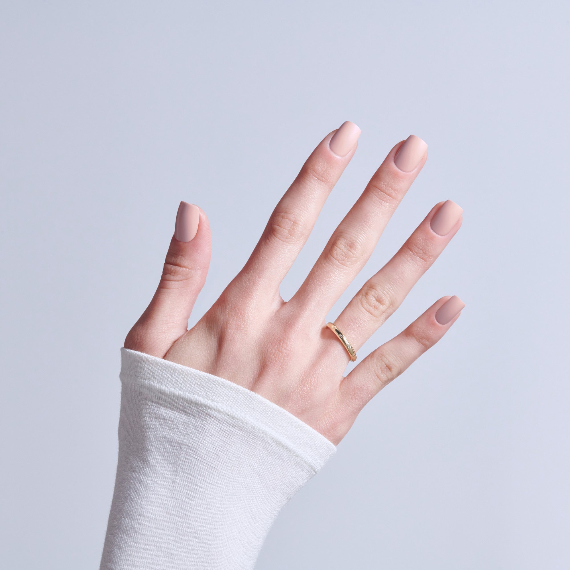 Hand with natural nude nails and gold ring on light background