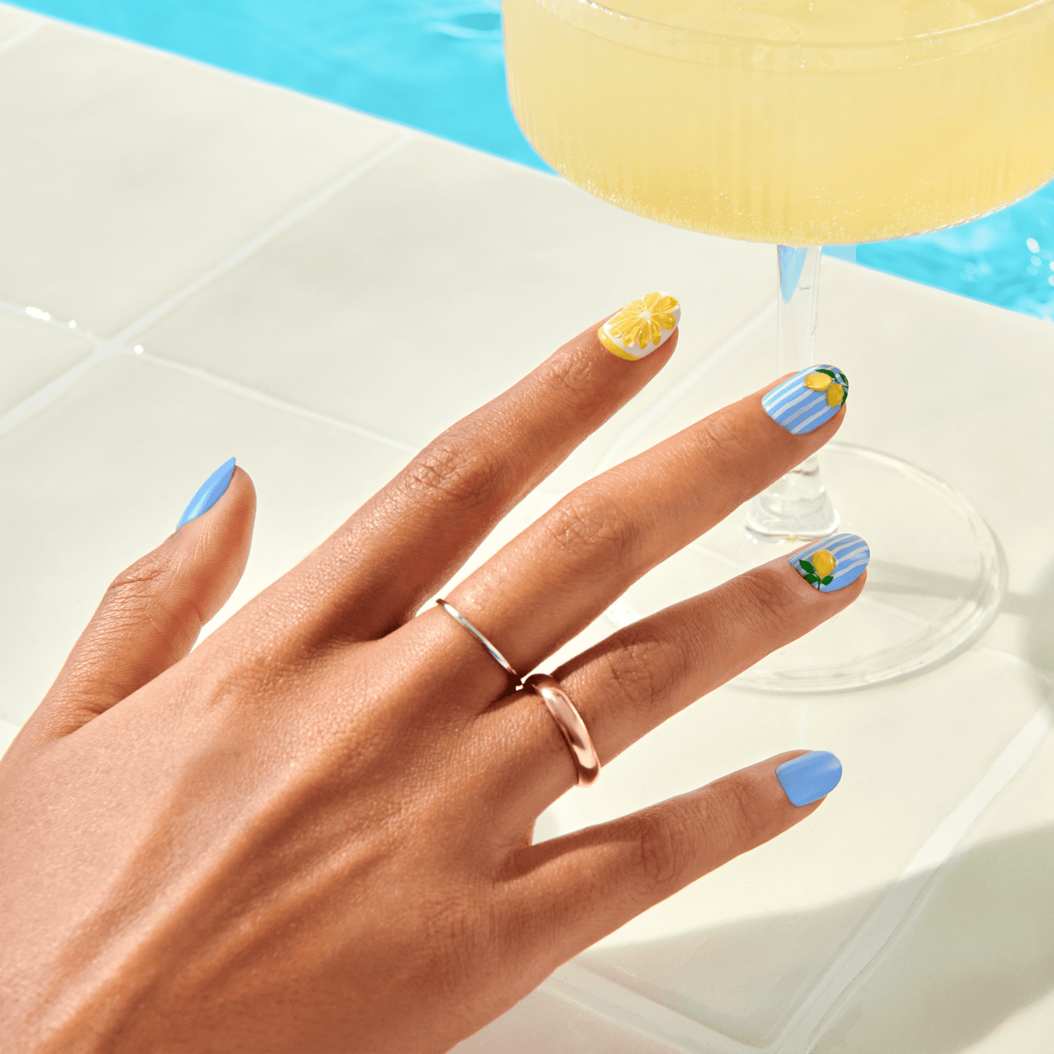 Hand with colorful nail art holding a cocktail on a pool float.