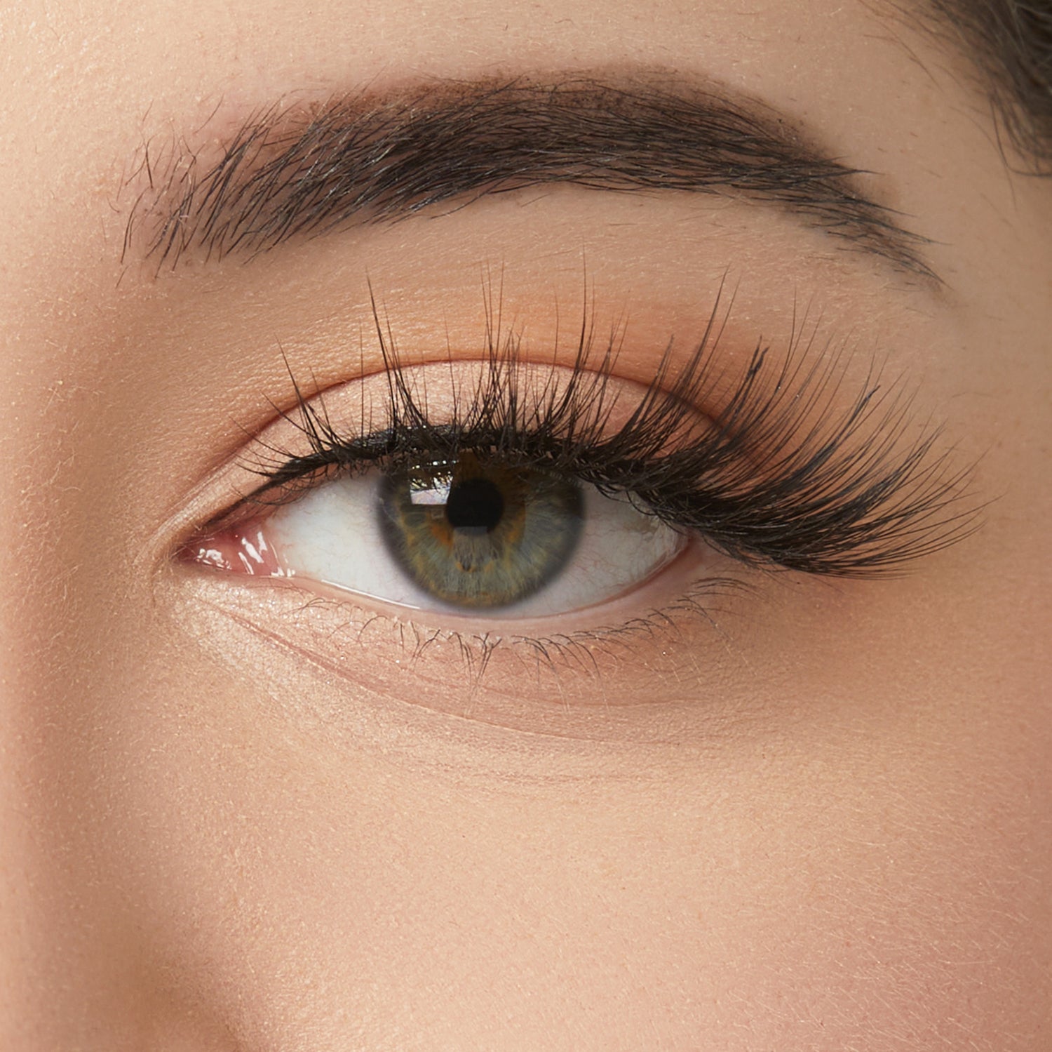 Close-up of eye with hazel iris, dark eyebrows, and black mascara on lashes.