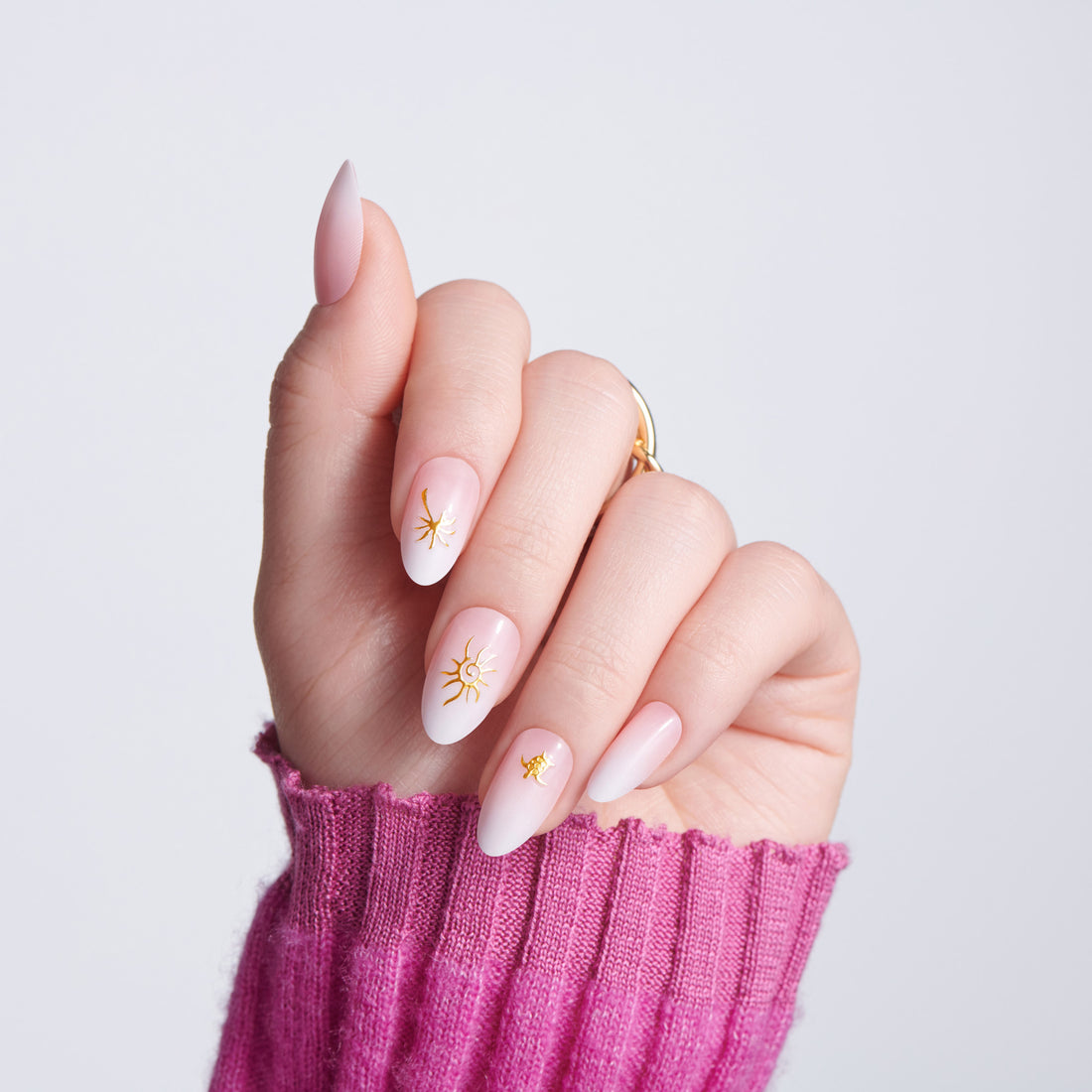 Hand with pink nail polish and gold star designs, wearing a pink sleeve against a light gray background