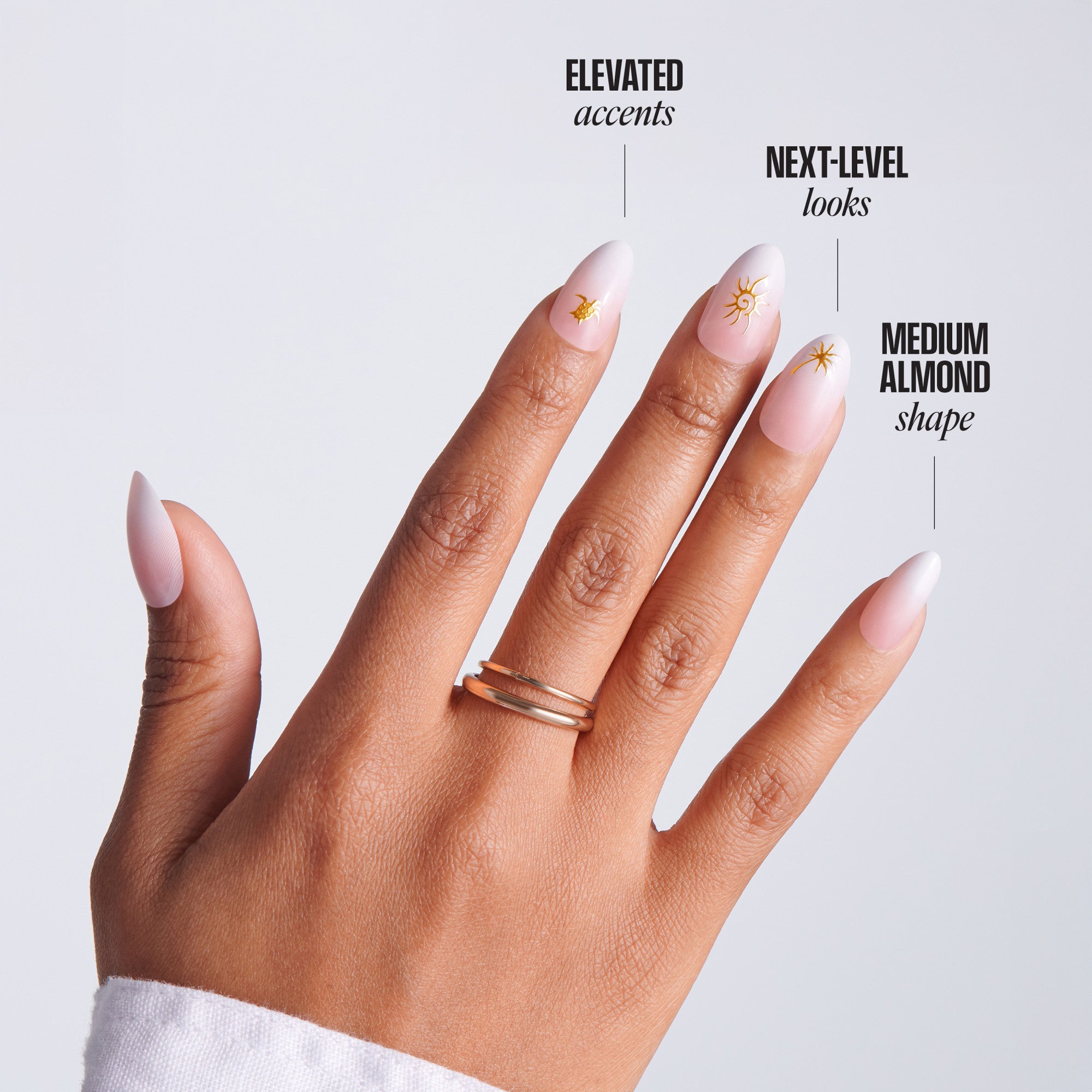Hand with medium almond-shaped nails and gold rings on a light gray background