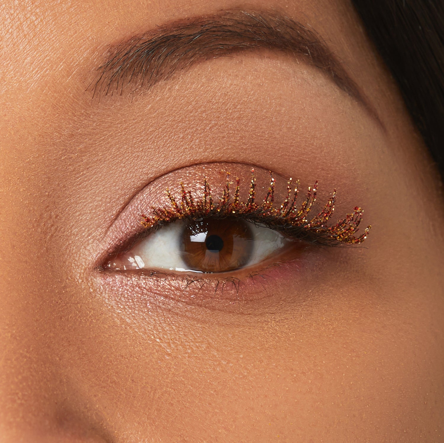 Close-up of eye with warm brown eyeshadow and gold glitter mascara