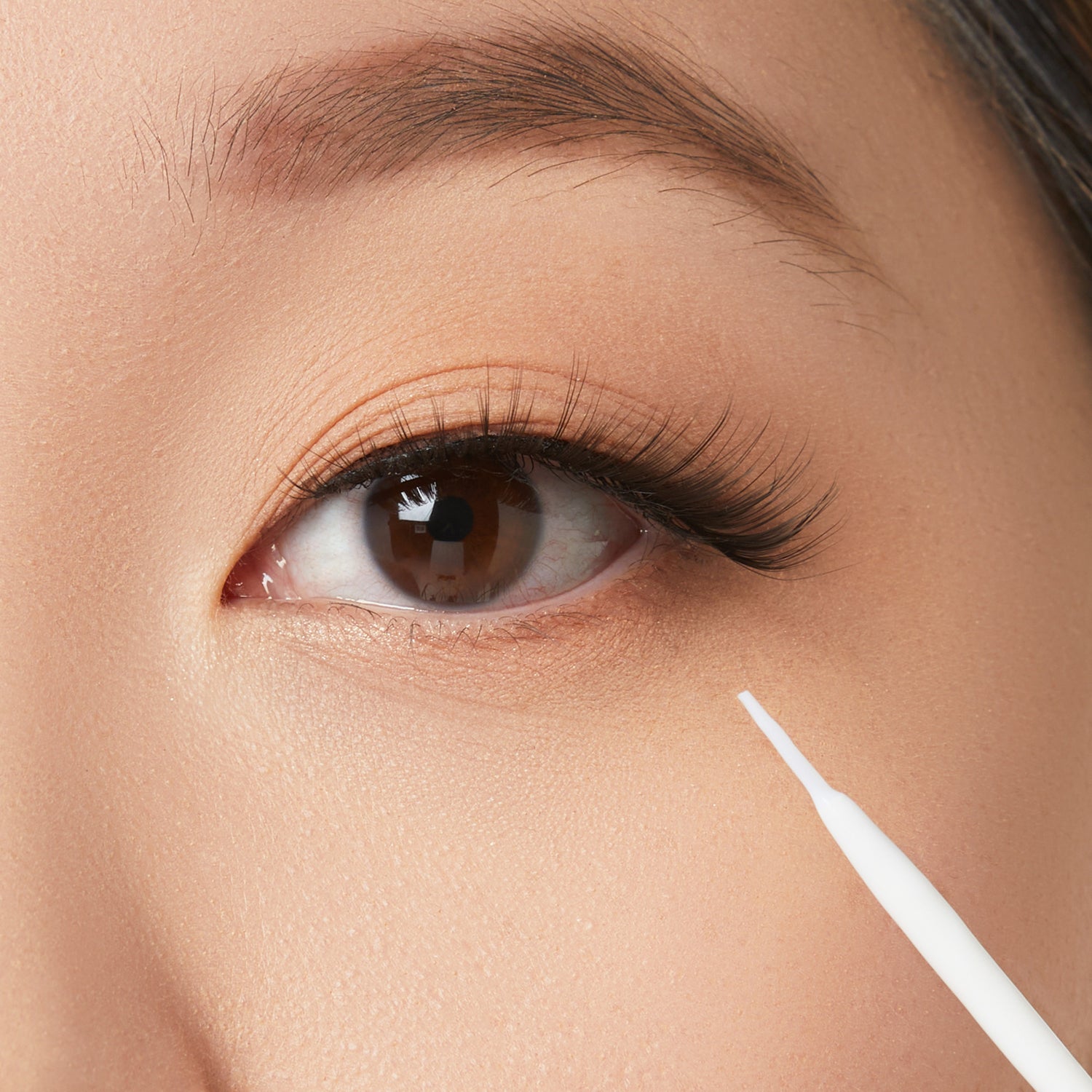 Close-up of eye makeup application with white eyeliner pencil on lower lash line.