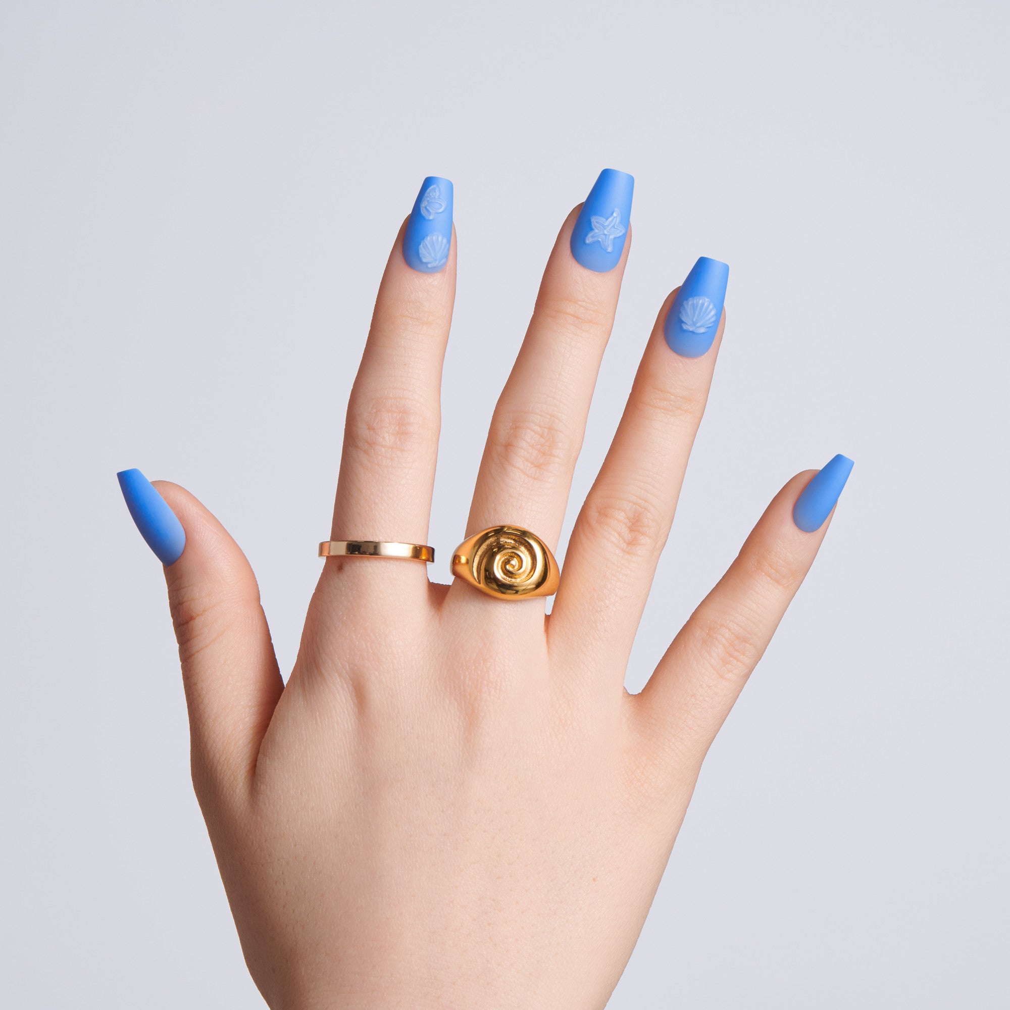 Hand with blue nail polish wearing a gold ring on a light gray background