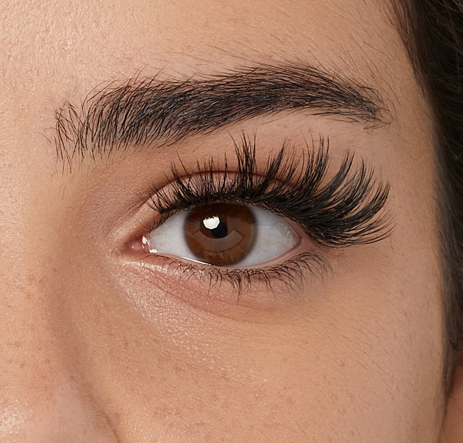 Close-up of eye with dark eyebrow and voluminous black mascara on lashes.