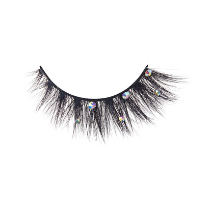 The image shows a single false eyelash. The eyelash is thick and voluminous with a dramatic, wispy design. It features several small, round, reflective rhinestones attached along the lash line, adding a touch of sparkle and glamour. The lash band is black and appears to be flexible for easy application.