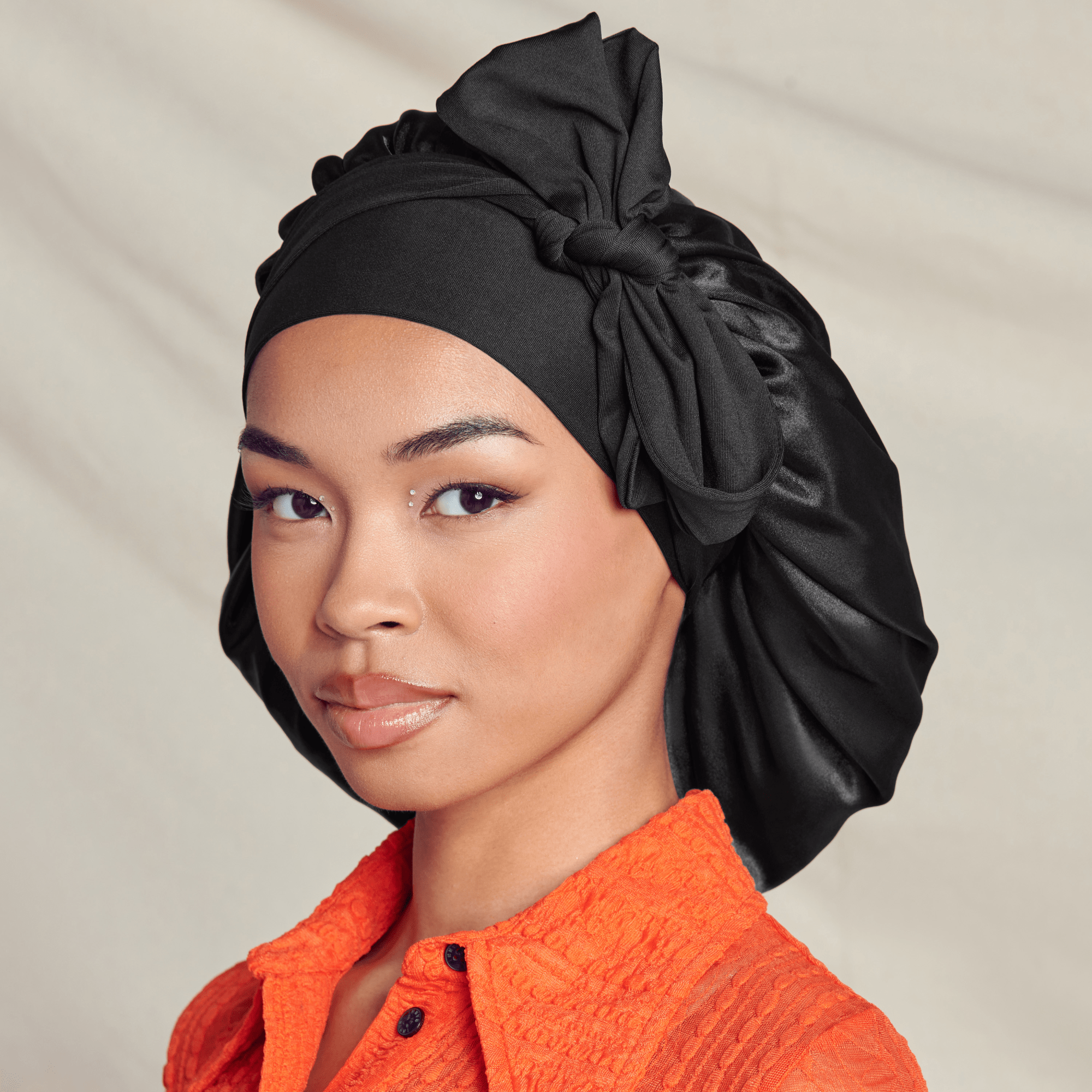 Woman wearing black head wrap and orange textured shirt, looking at camera.